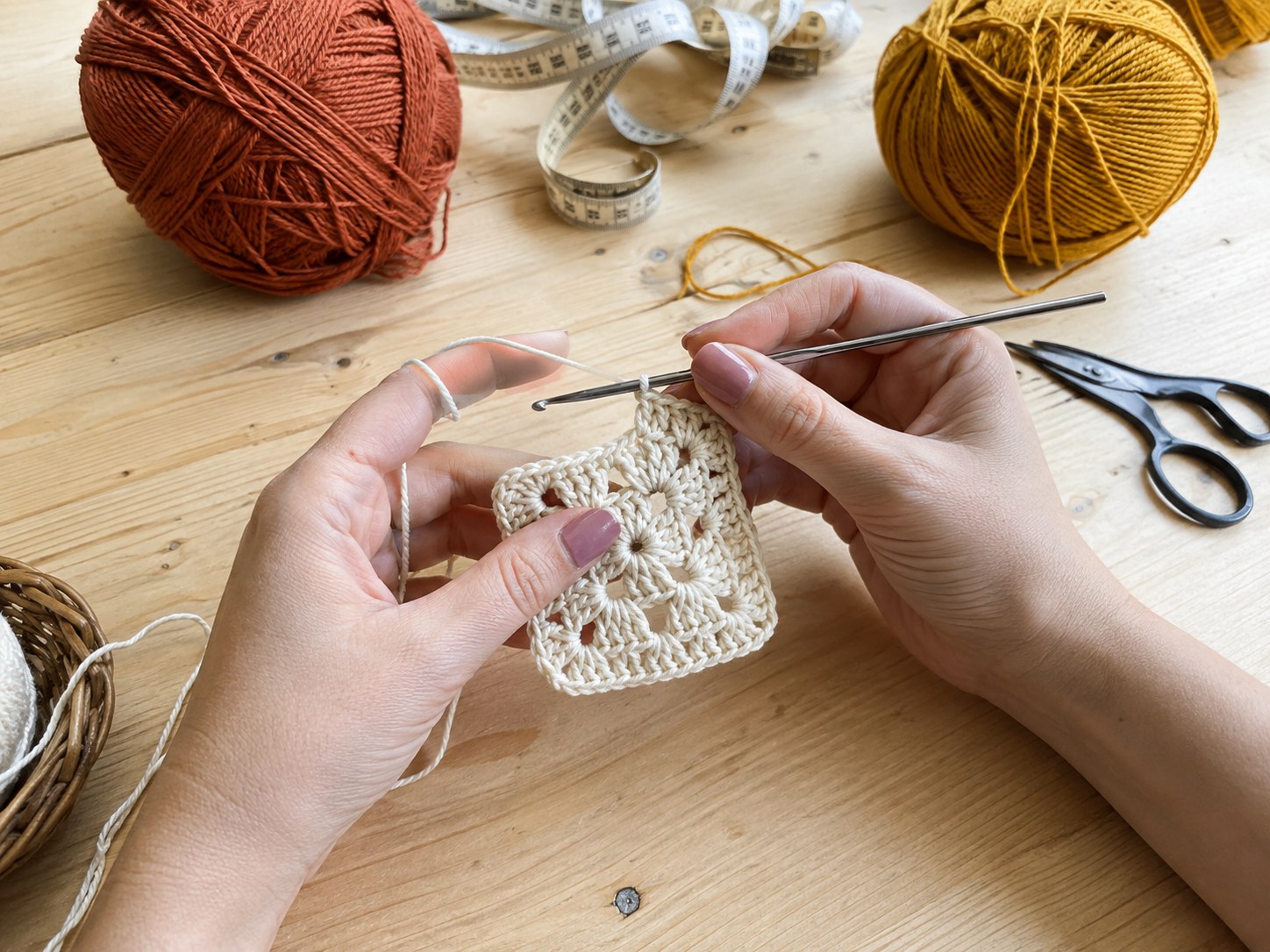 Hands crocheting a small test granny square swatch on a wooden table
