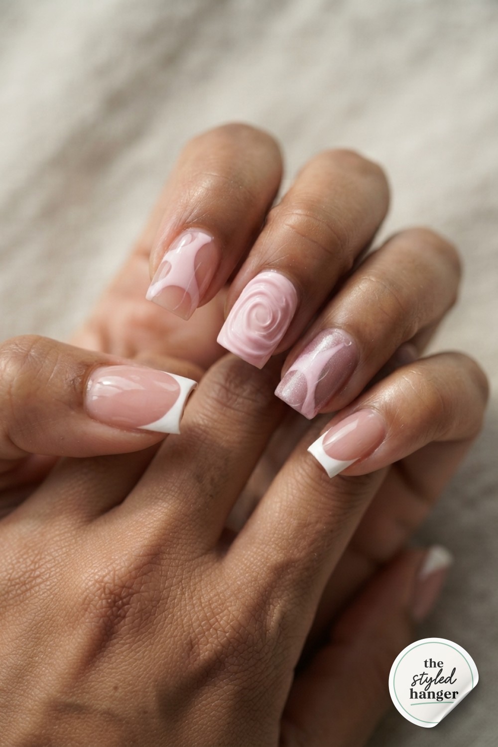 A two-tone pink French tip design decorates short oval nails resting on a satin pillow.