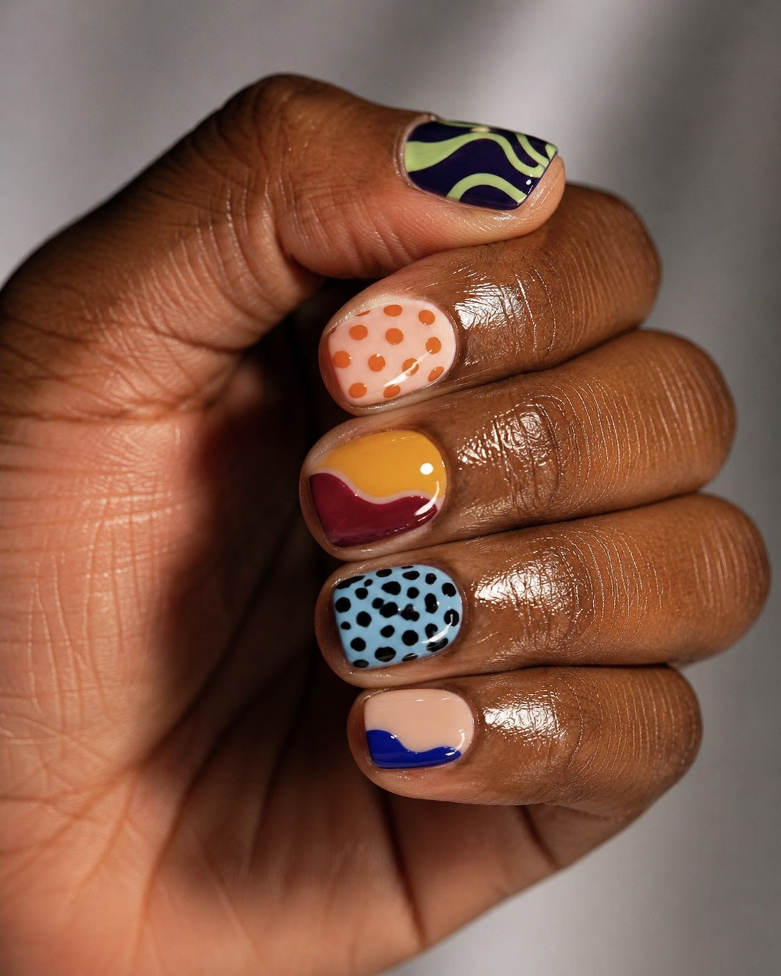 Mismatched abstract nail art in warm tones on short natural nails