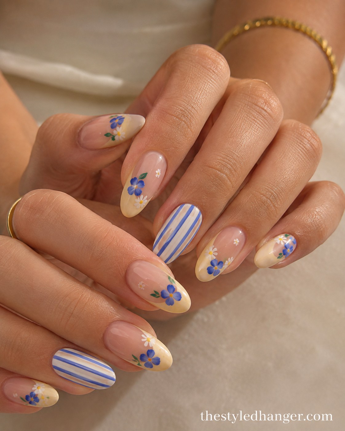 Cream nails with hand-painted blue floral French tips, a summer nail color for dark skin