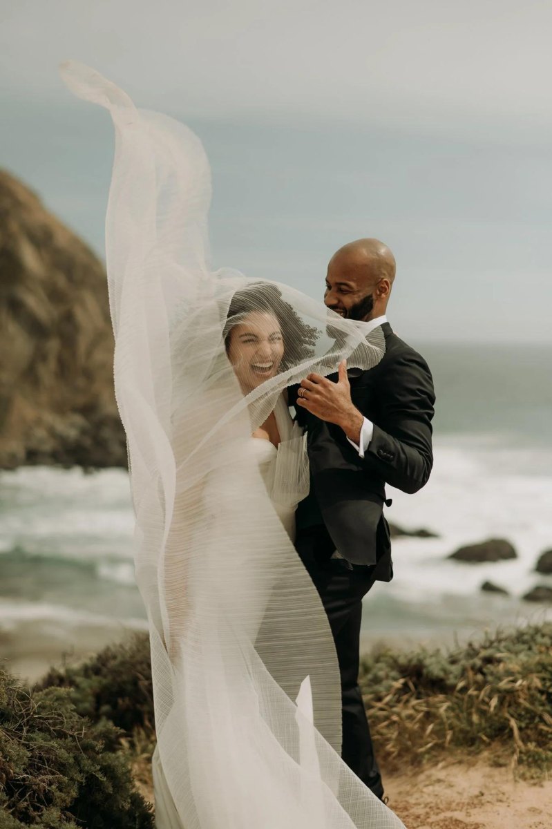 Bride and groom with flowing veil coastal elopement pose
